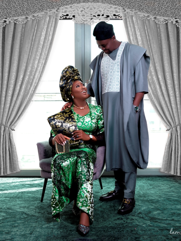 Couple In Vibrant Green Traditional Outfits Posing Indoors, With The Woman Seated And The Man Standing Beside Her.